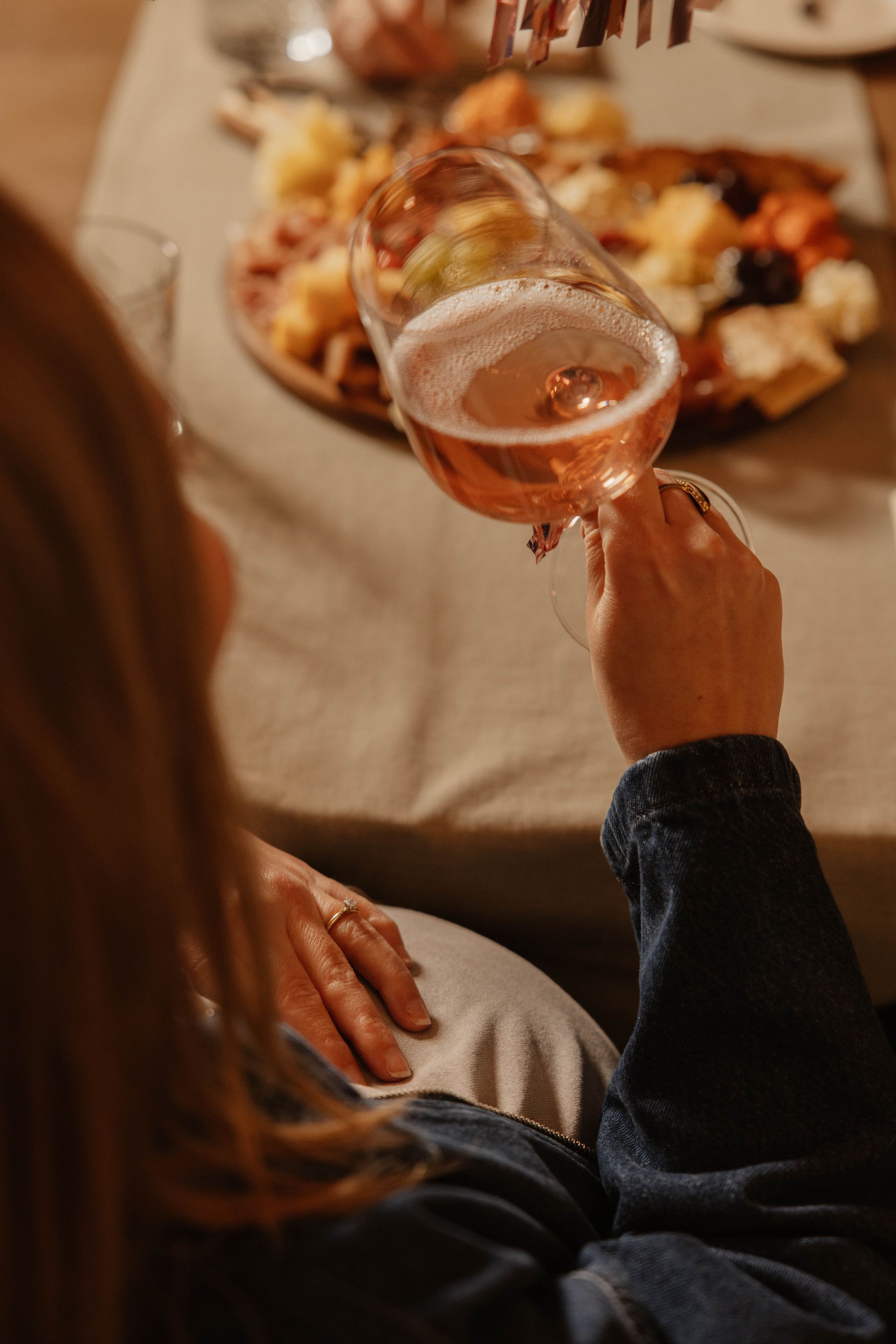 Iemand die zwanger is en proost met een glas alcoholvrije bubbel aan een eettafel met hapjes.