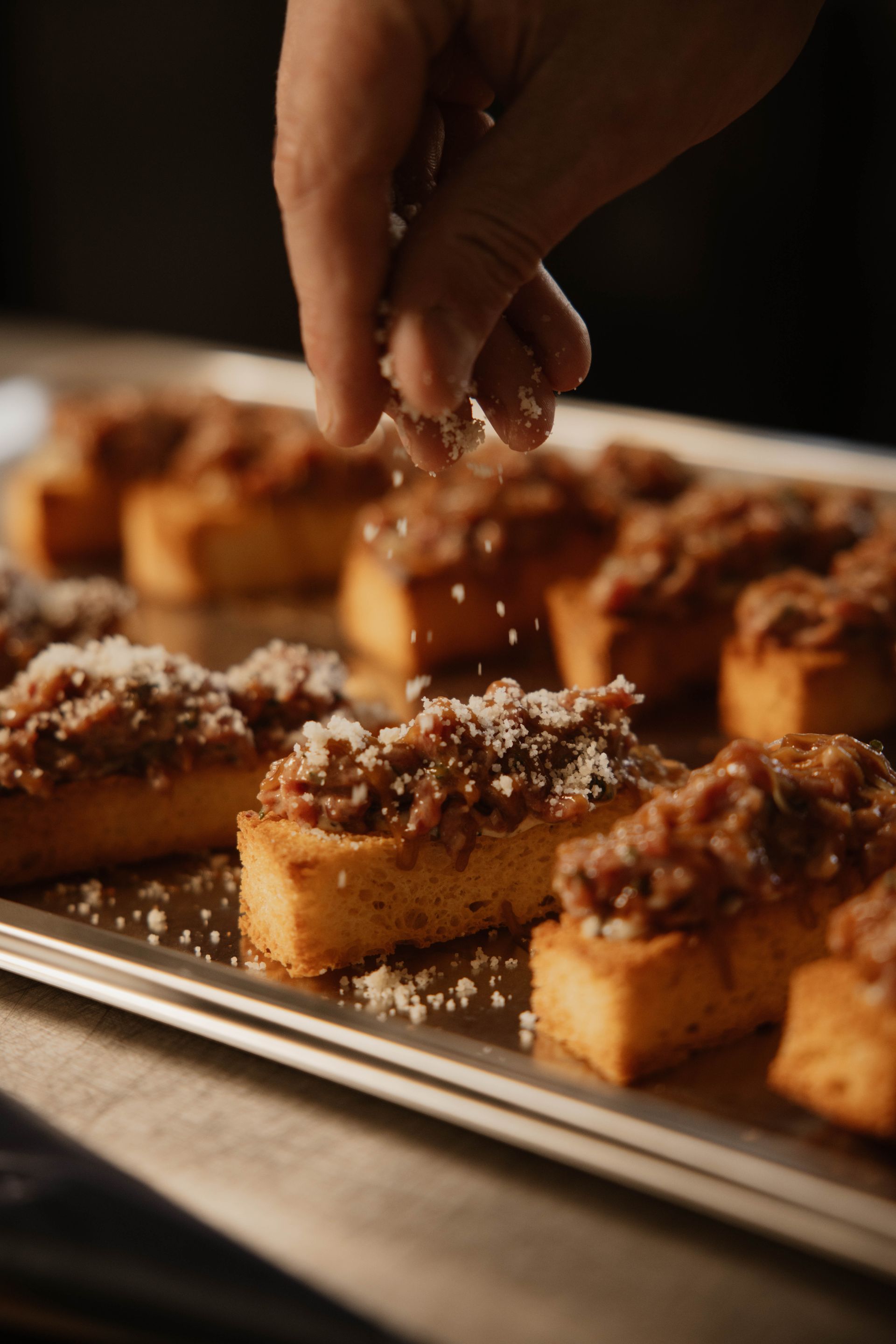 Een huisgemaakt briochebrood waar steak tartaar op zit en waar met een hand parmezaanse kaas op gestrooid wordt.