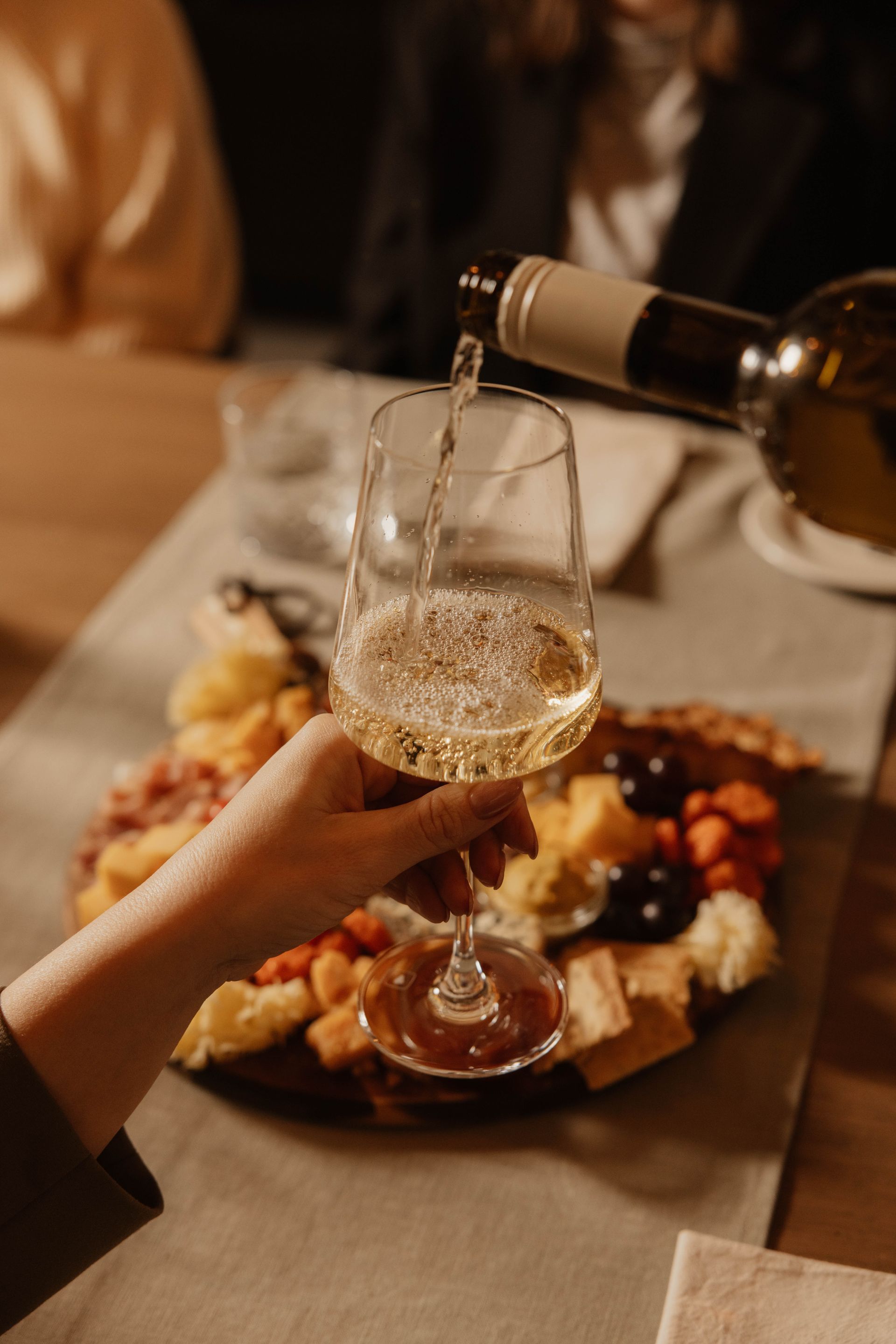 Het met de hand inschenken van witte wijn in een glas aan een eettafel, met voorgerechten en een ander glas in de buurt.