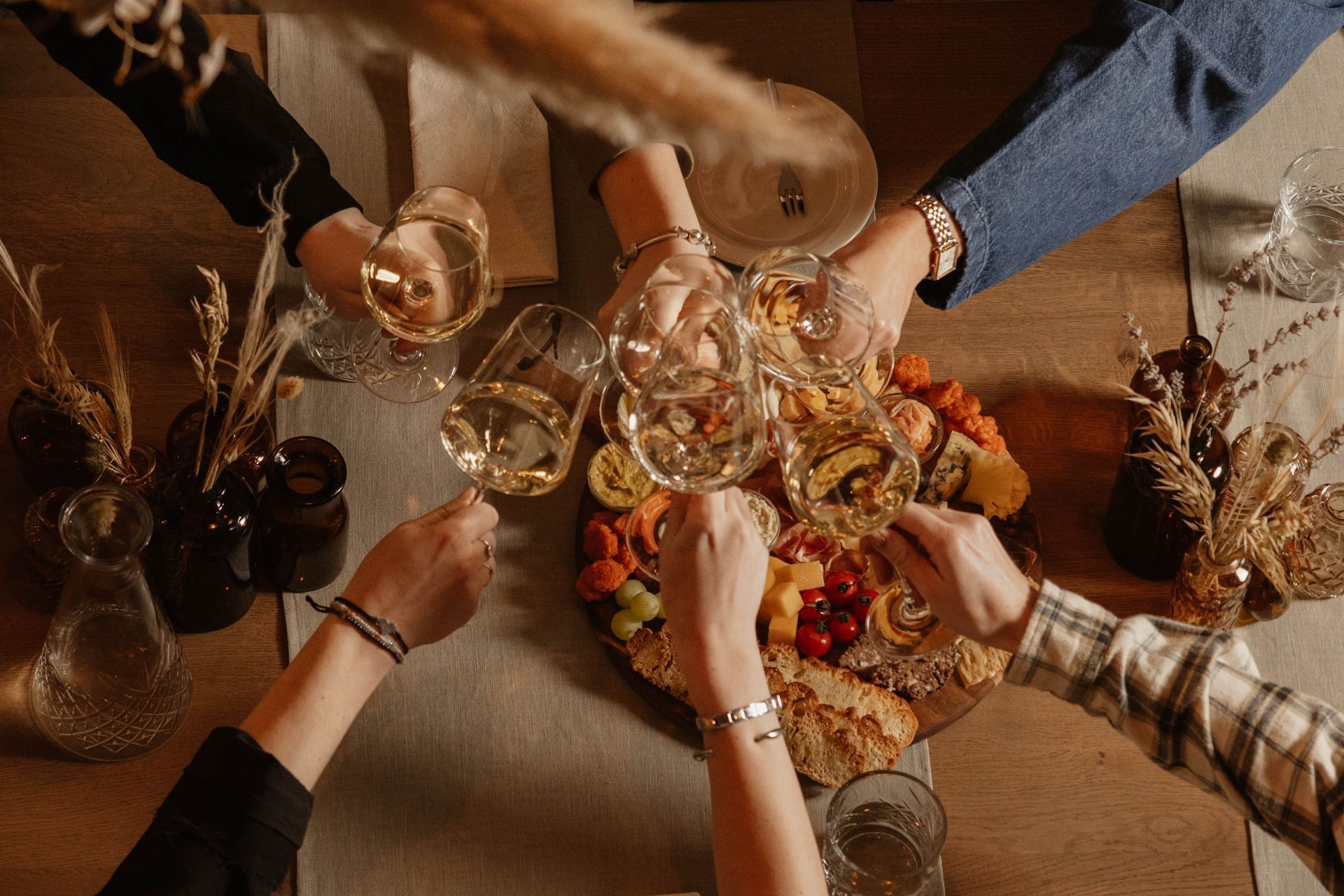 Vrienden klinken het glas bij een gezamenlijke borrel aan een warme, rustieke tafel, met kaarsen en decoratie.