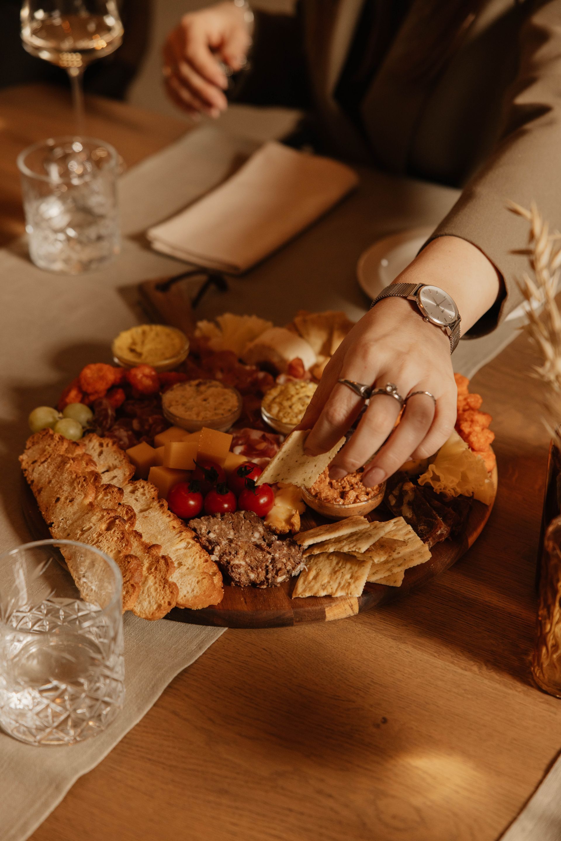Iemand die wat lekkers pakt van een plank vol met kazen en charcuterie.