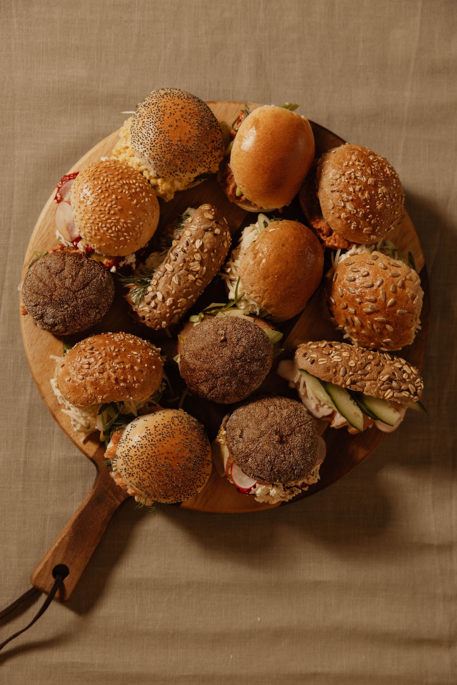 Een houten plank met diverse broodjes en -bolletjes op een beige tafelkleed.