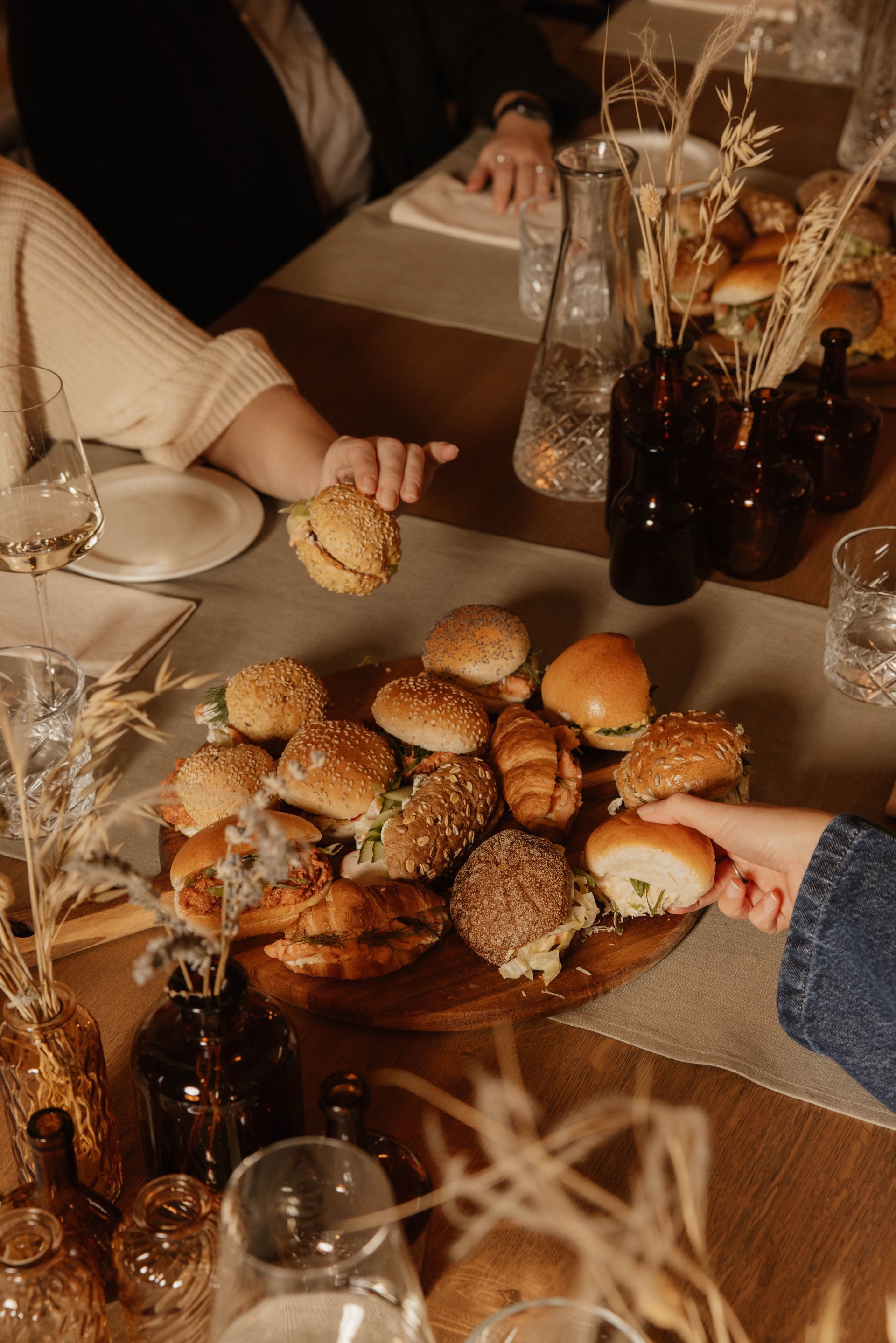 Een schaal met sandwiches wordt geserveerd aan een tafel met drankjes en decoraties van gedroogde bloemen.