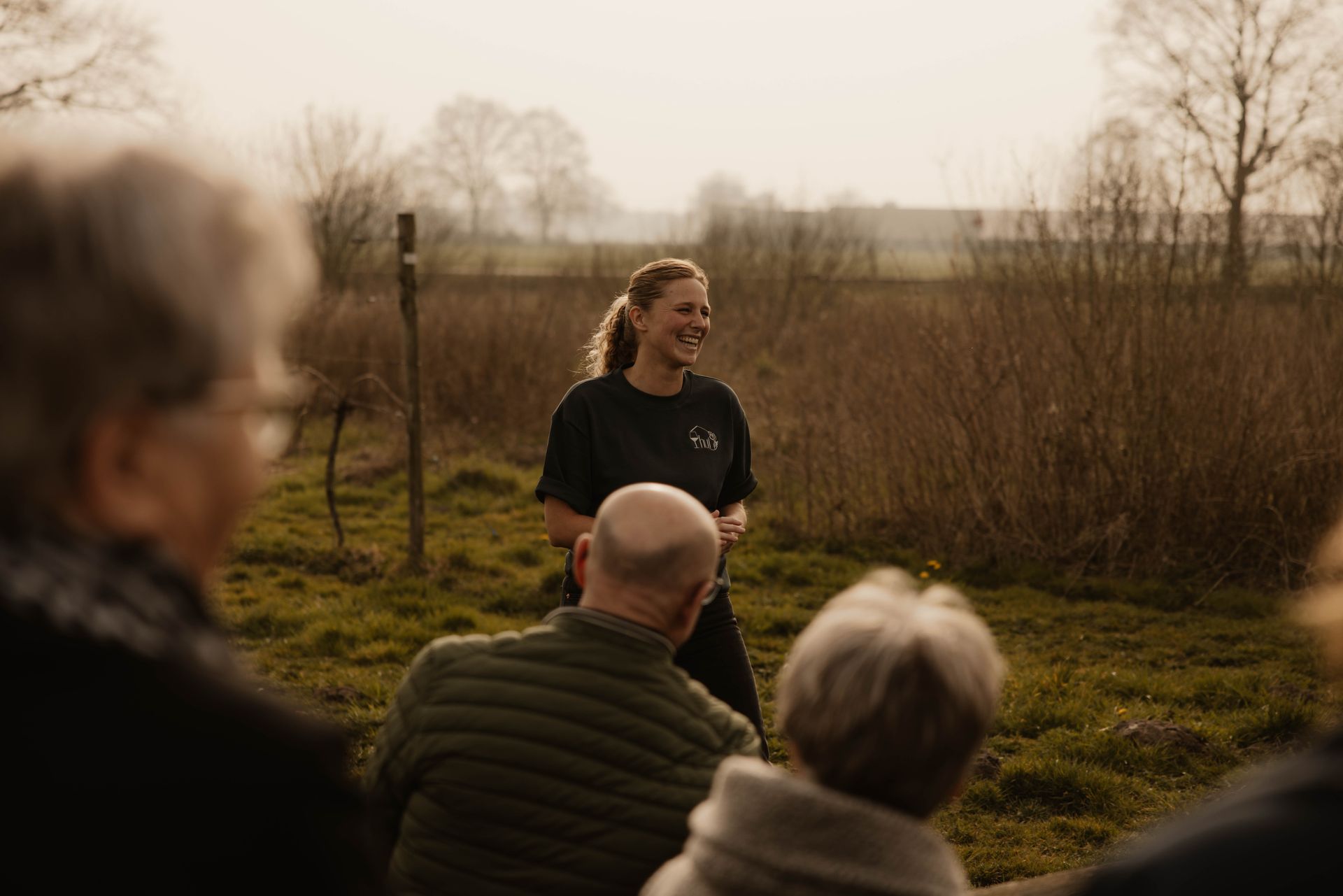 Een kleine groep luistert naar een spreker in de buitenlucht, in een wijngaard.