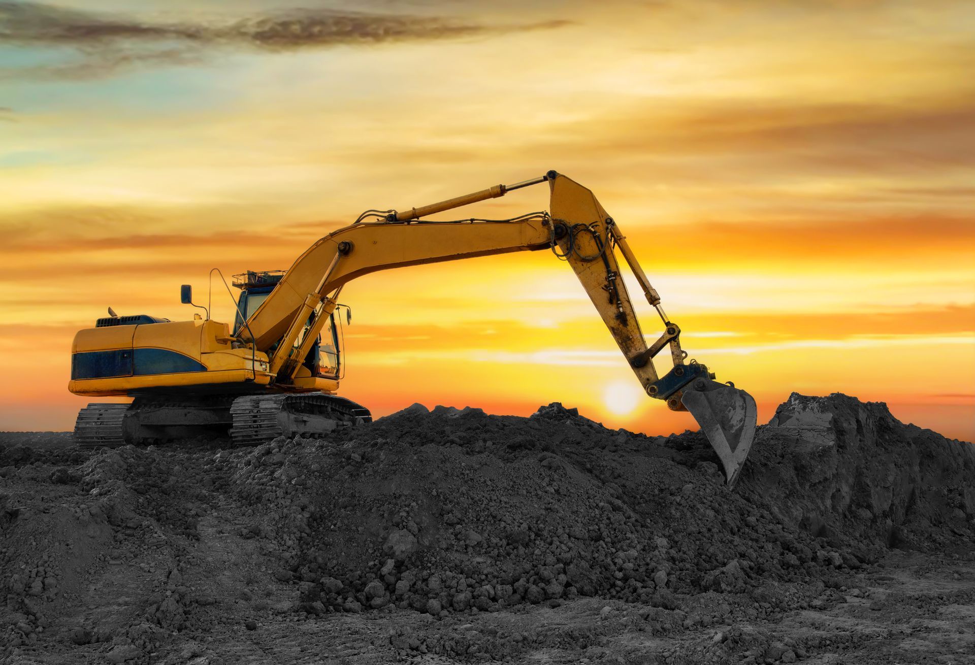 Yellow excavator on a pile of dirt against a sunset sky.