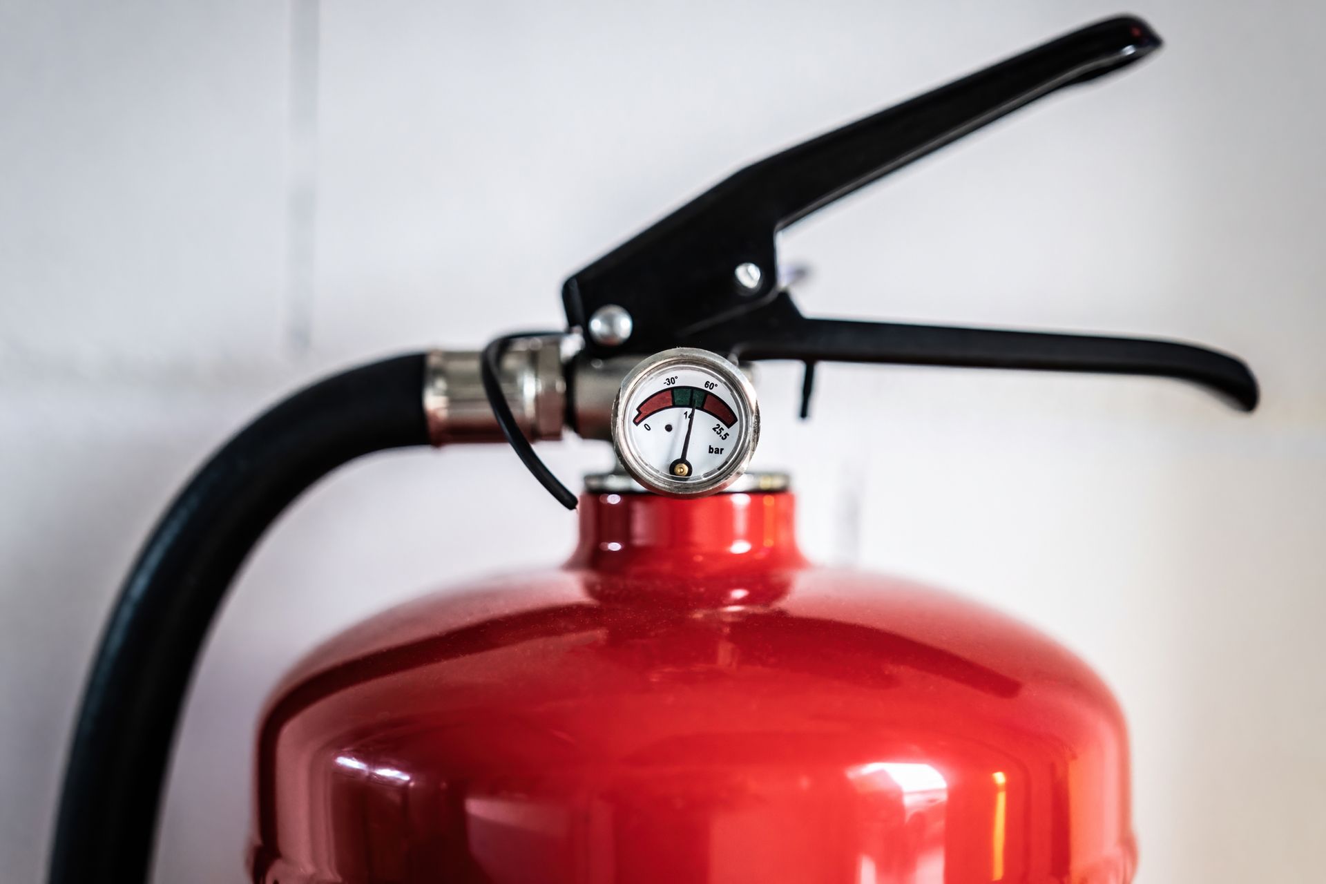 A close up of a red fire extinguisher against a white wall. A close up of a red fire extinguisher against a white wall.