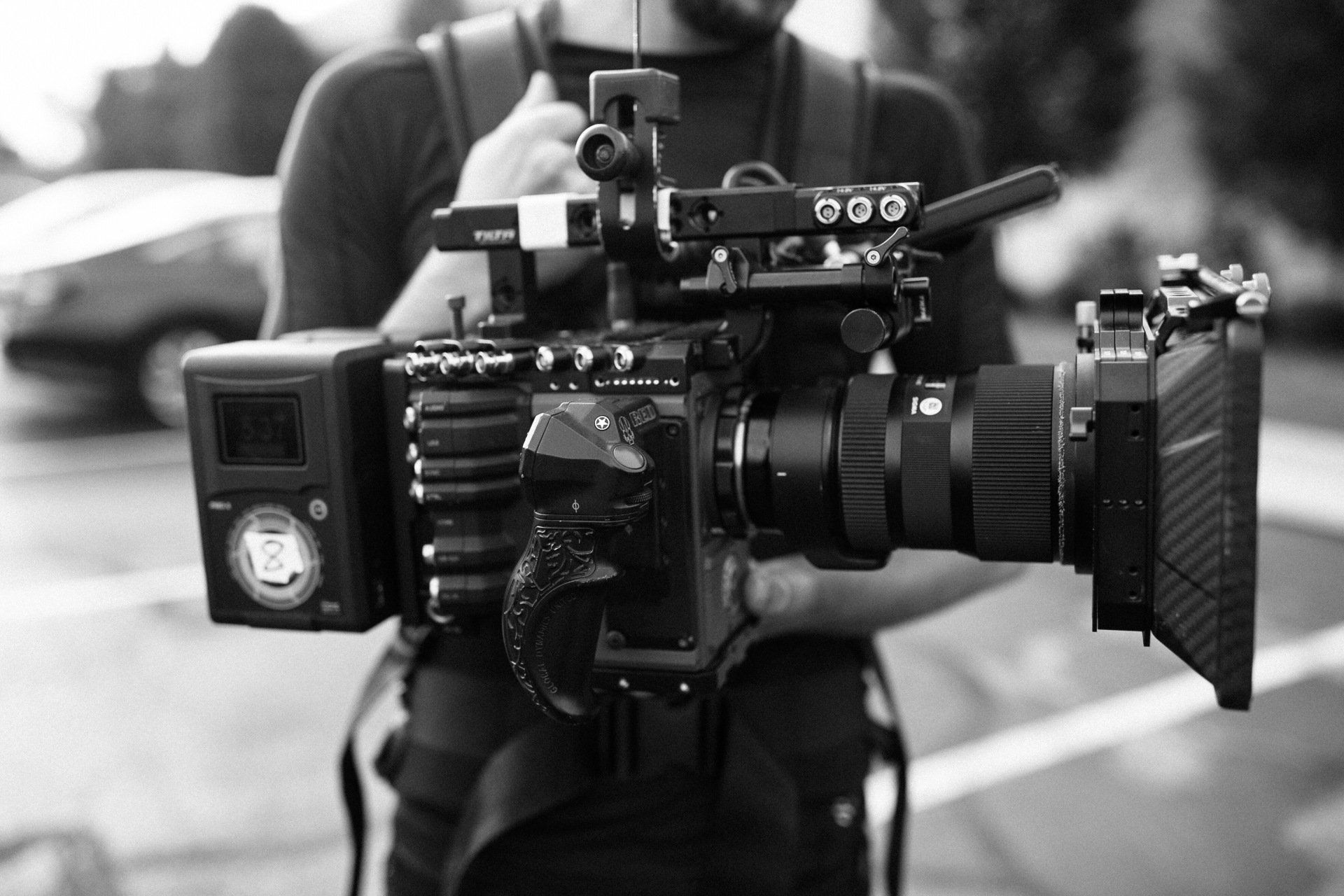 Persoon met een professionele videocamera met een grote lens en matte box, zwart-wit close-up.