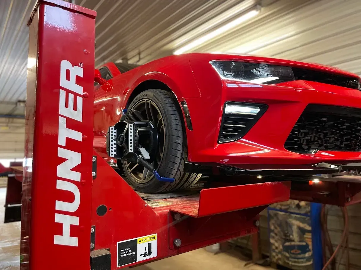 Red sports car on a red Hunter alignment lift. Tire alignment equipment attached to front wheel | Chet's Wheel Alignment