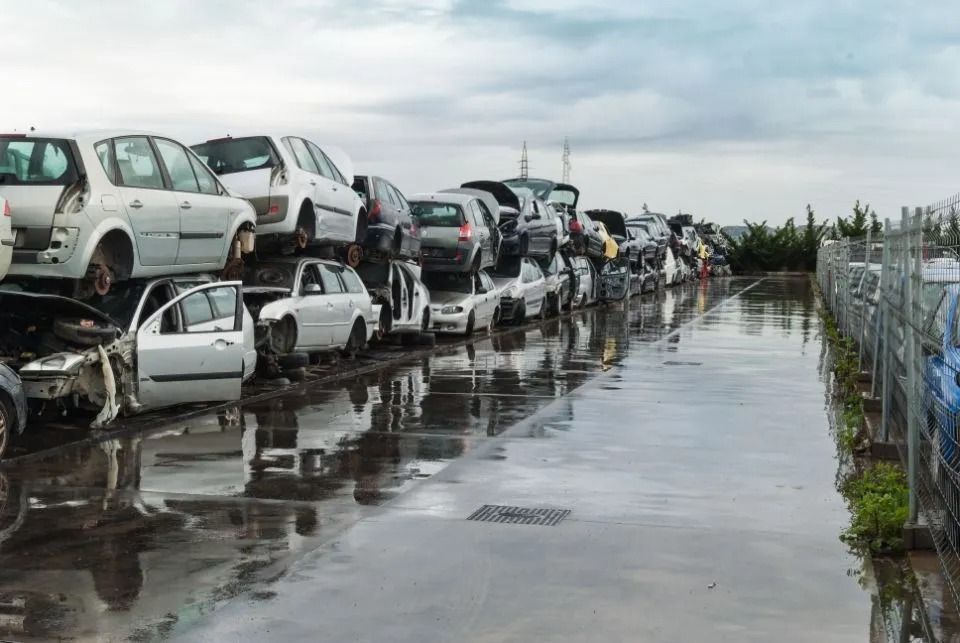 Rows of wrecked cars stacked at a junkyard on a wet, overcast day.