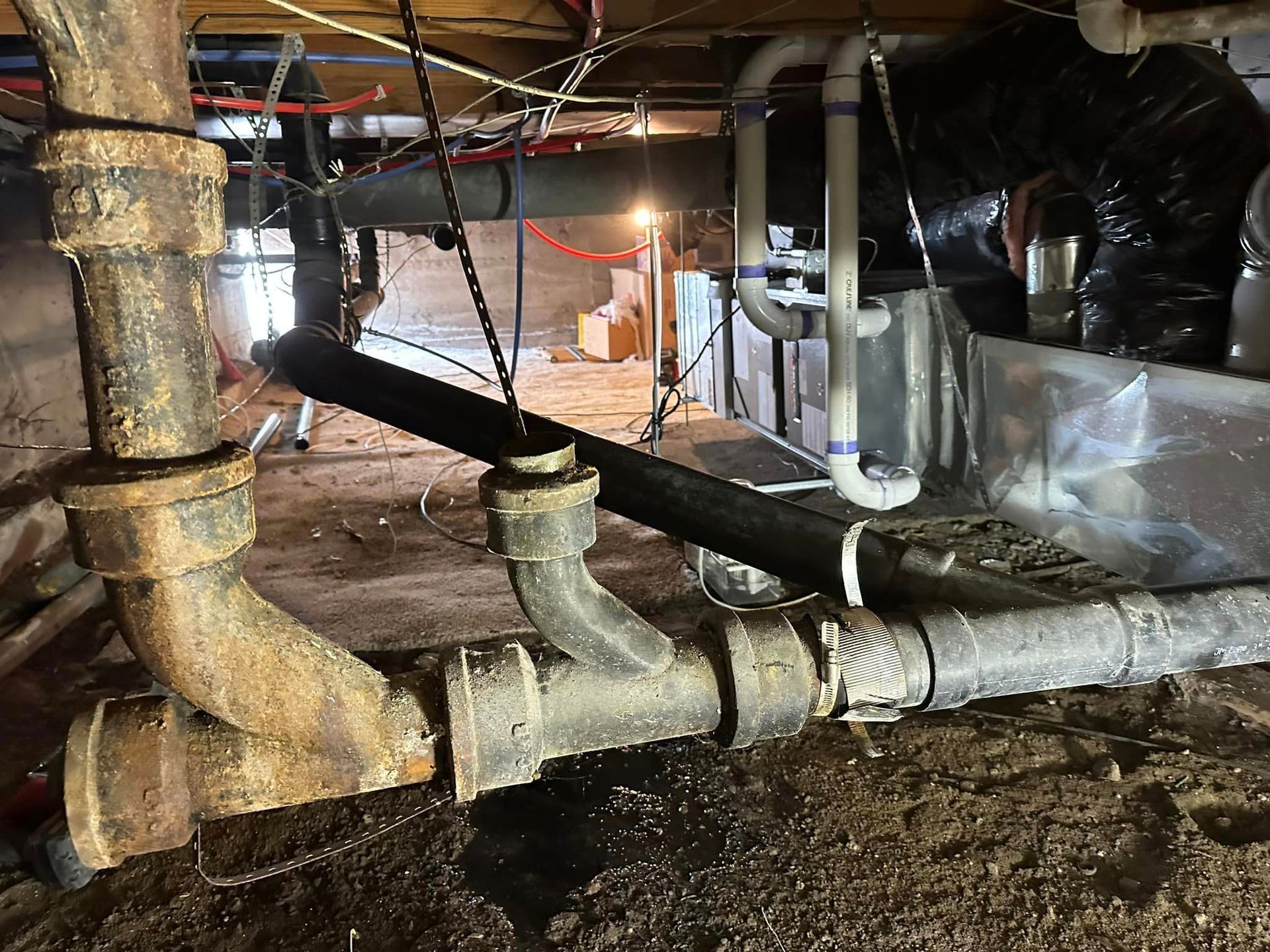 A bunch of pipes are hanging from the ceiling in a basement.