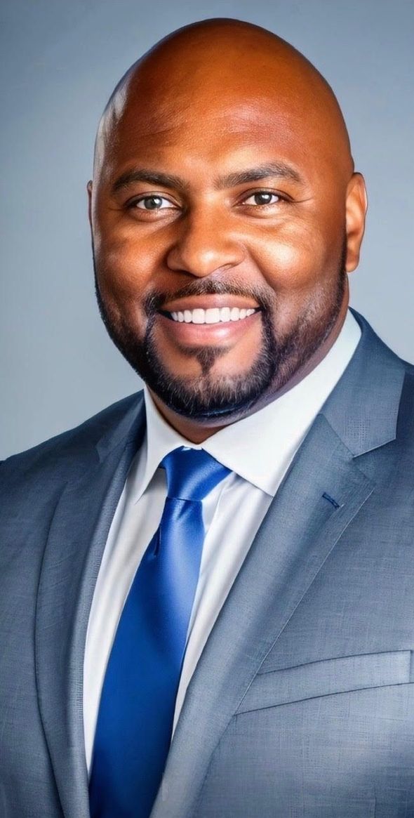 Professional headshot of a smiling man in a gray suit with a blue tie against a blue-gray background