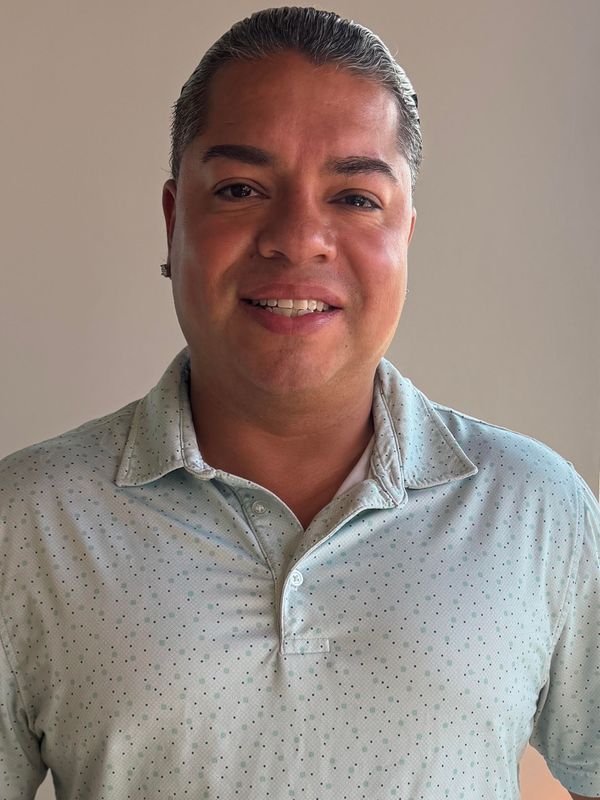 Smiling person in a light patterned shirt against a plain wall.