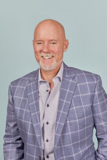 Smiling bald man in a gray plaid blazer and light shirt against a pale blue background
