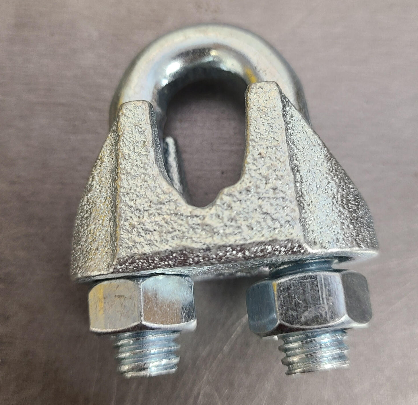 Metal wire rope clip with two bolts on a gray surface