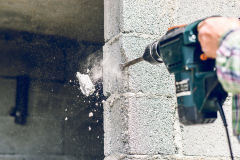 Person drilling into a cinder block wall, with dust and debris flying.
