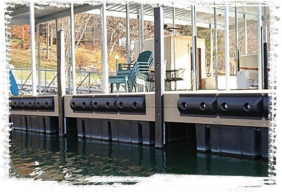 Covered lakeside dock with green chairs, railings, and water below