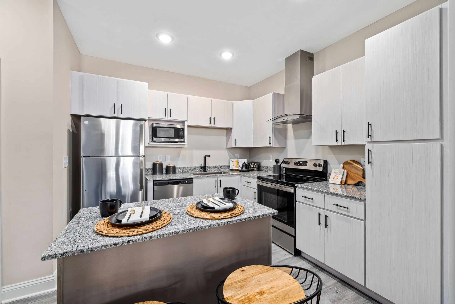 Modern kitchen with white cabinets, stainless steel appliances, and a granite island table set for two