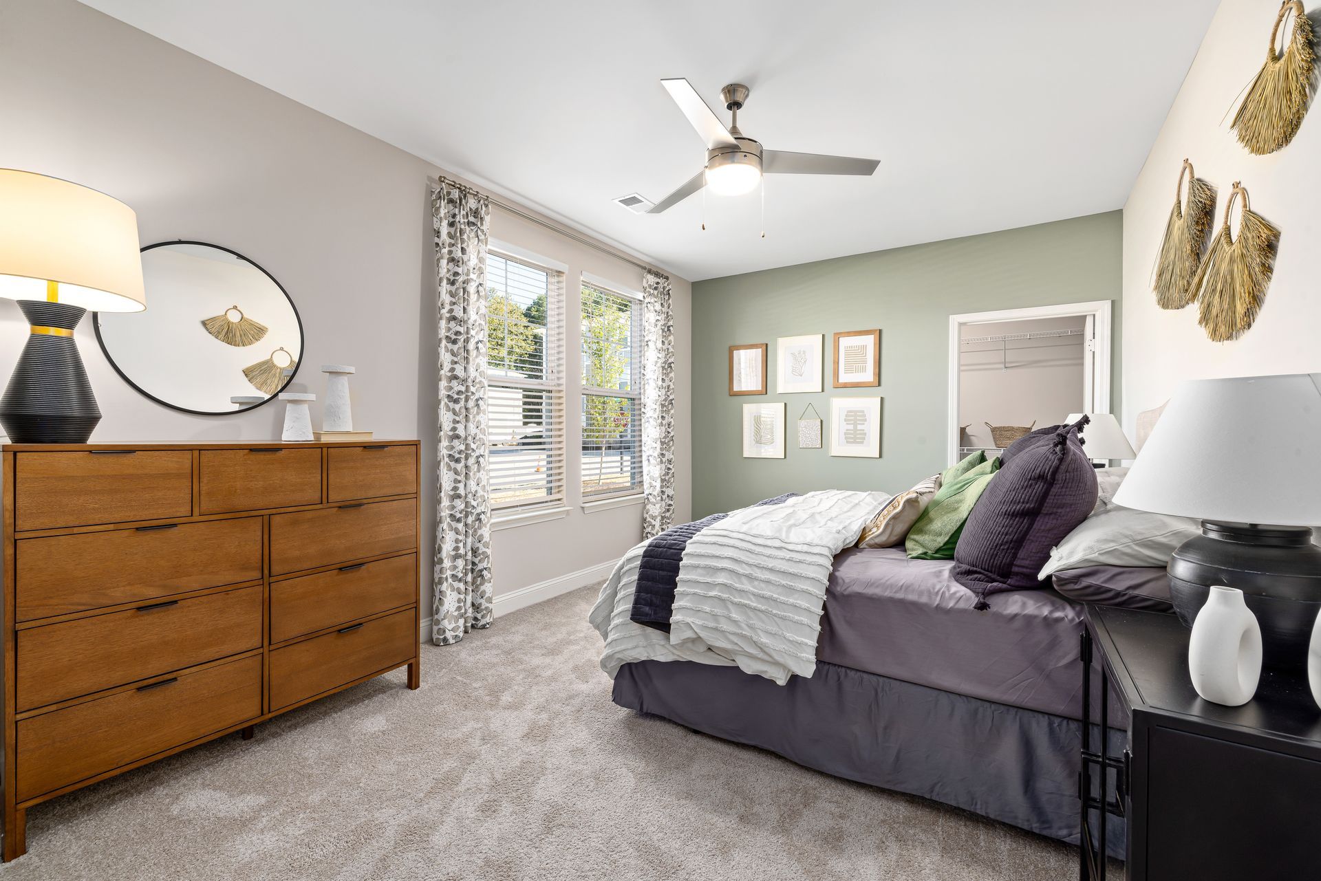 Bright bedroom with gray bedspread, wooden dresser, green accent wall, and window with blinds