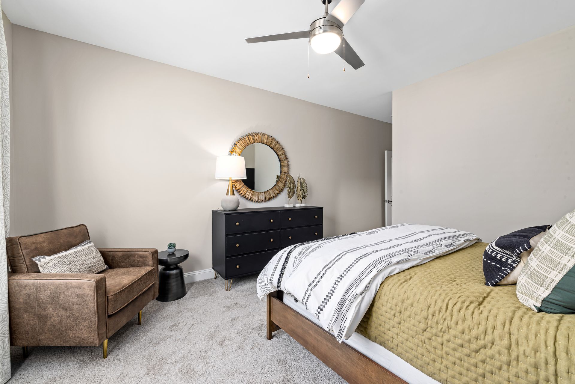 Bright bedroom with gray walls, bed, armchair, dresser, and ceiling fan