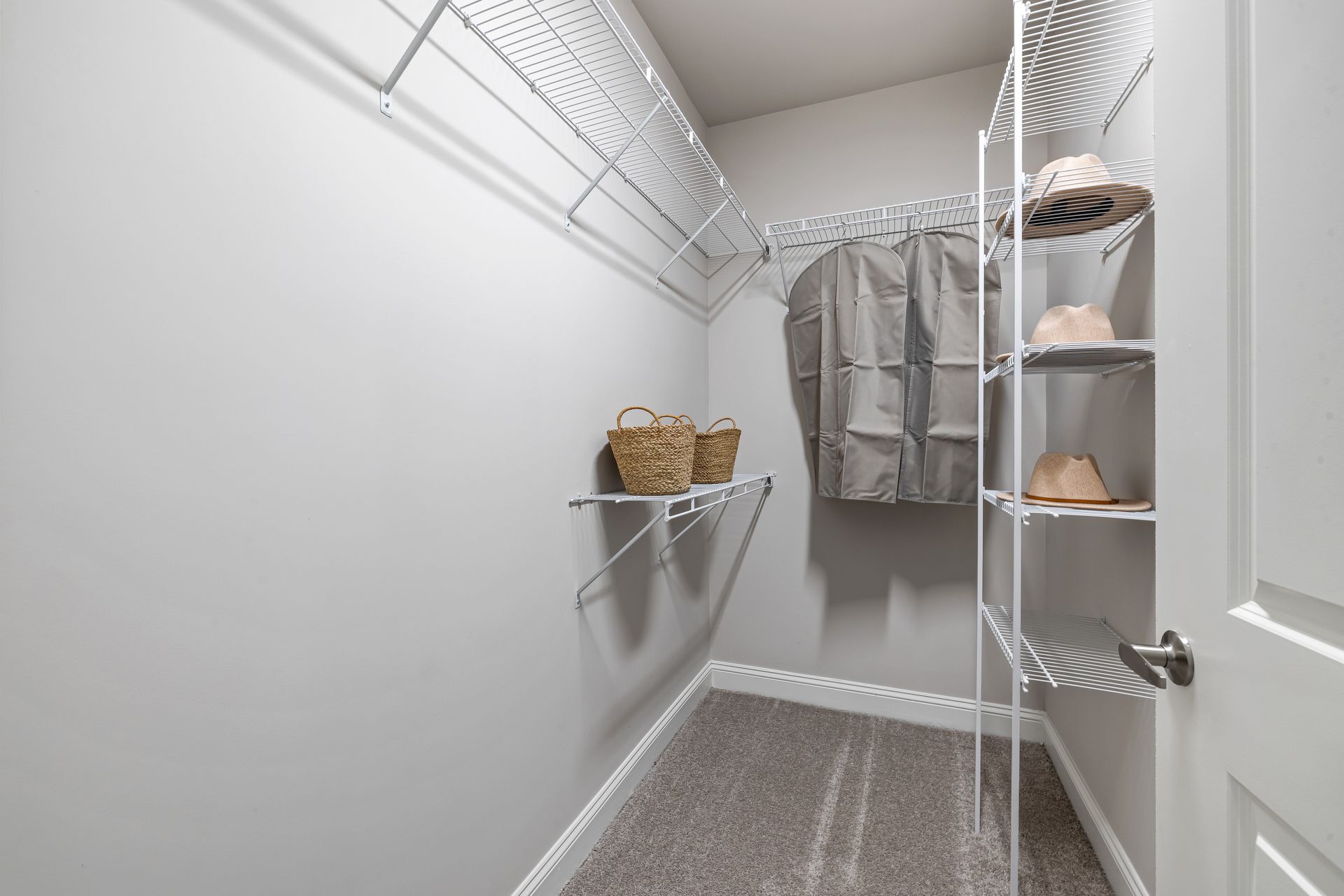Walk-in closet with wire shelving, hanging clothes, baskets, and shoes on a gray carpet.