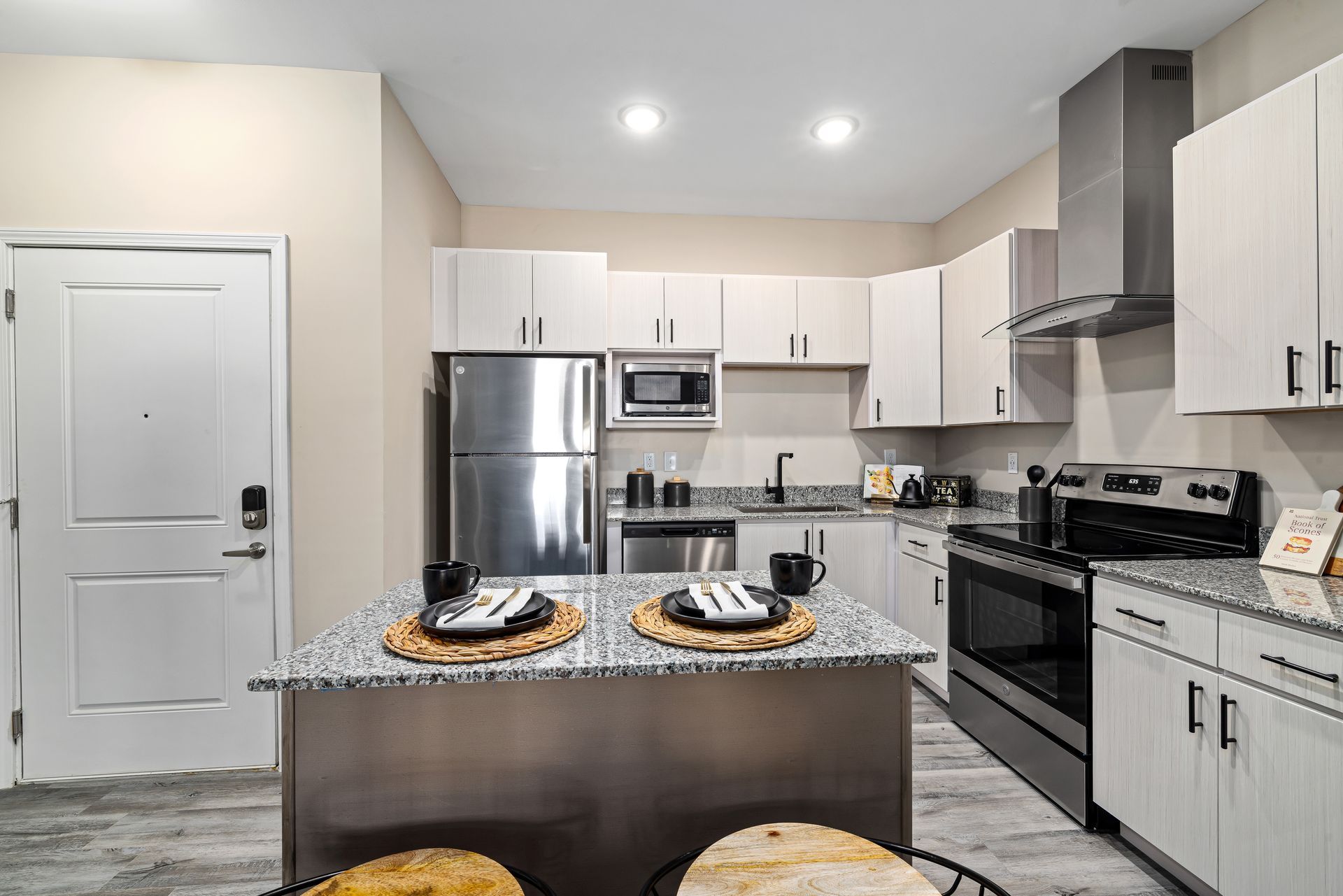 Modern kitchen with stainless steel appliances, granite island, and place settings on the counter