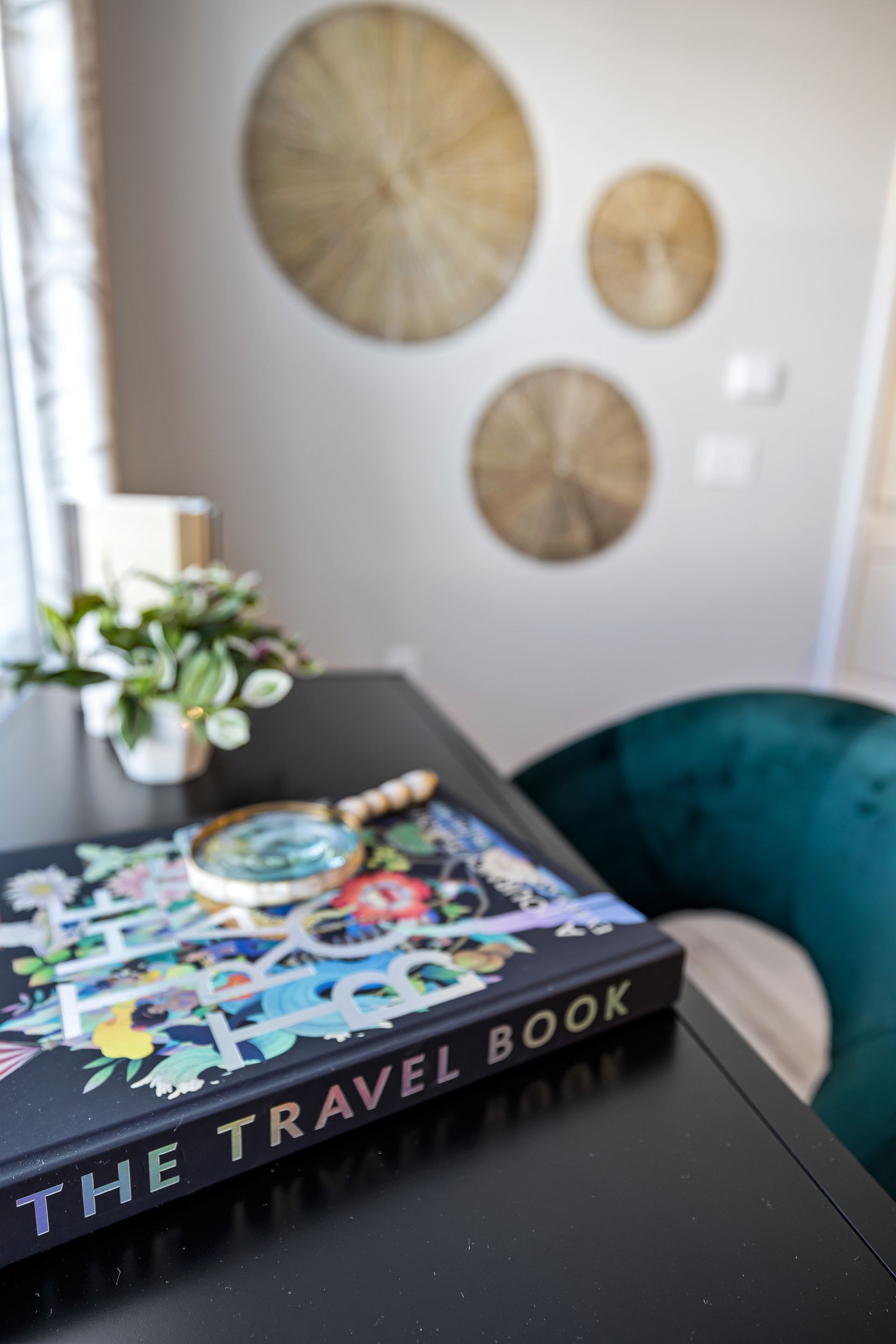 Travel book on a black table with a small plant, teal chair, and wall decor in a cozy room