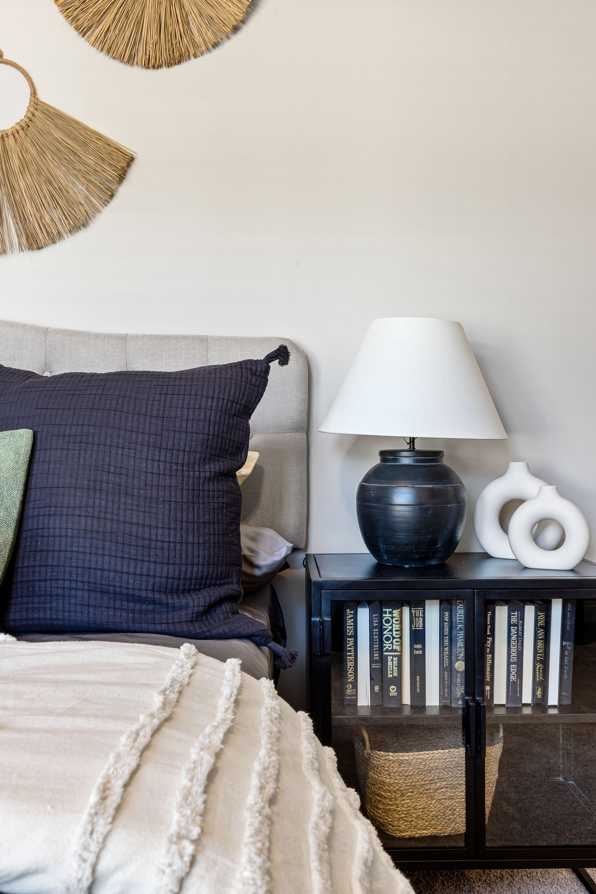 Cozy bedroom corner with bed, navy pillow, table lamp, and black shelf with books and decor