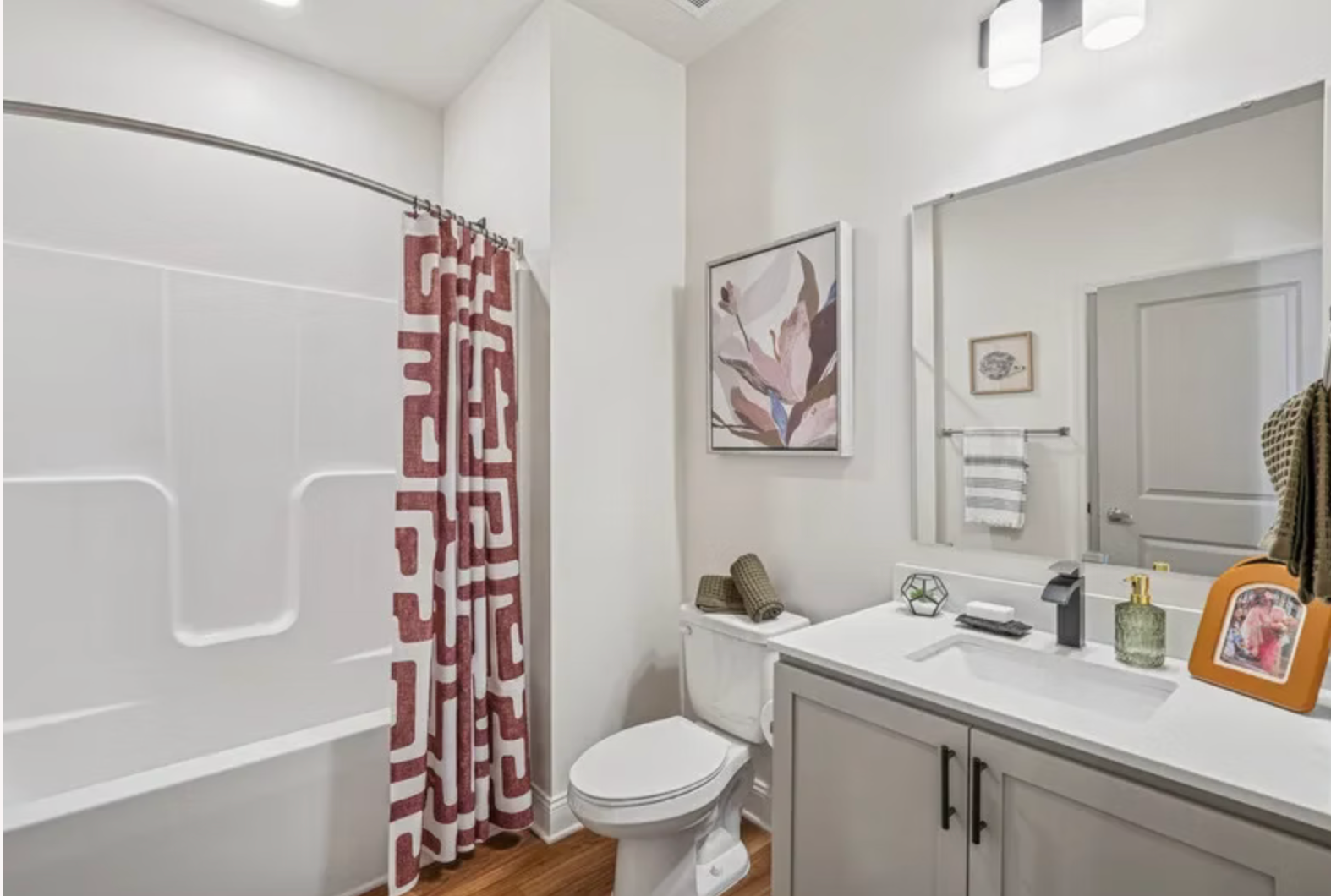 Bright bathroom with white tub, red patterned shower curtain, toilet, and vanity with mirror