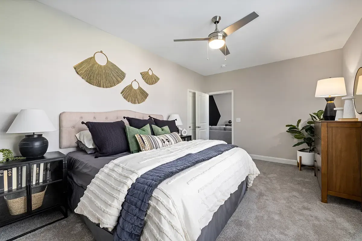 Cozy bedroom with gray bed, white bedding, ceiling fan, and dresser in a neutral-toned room