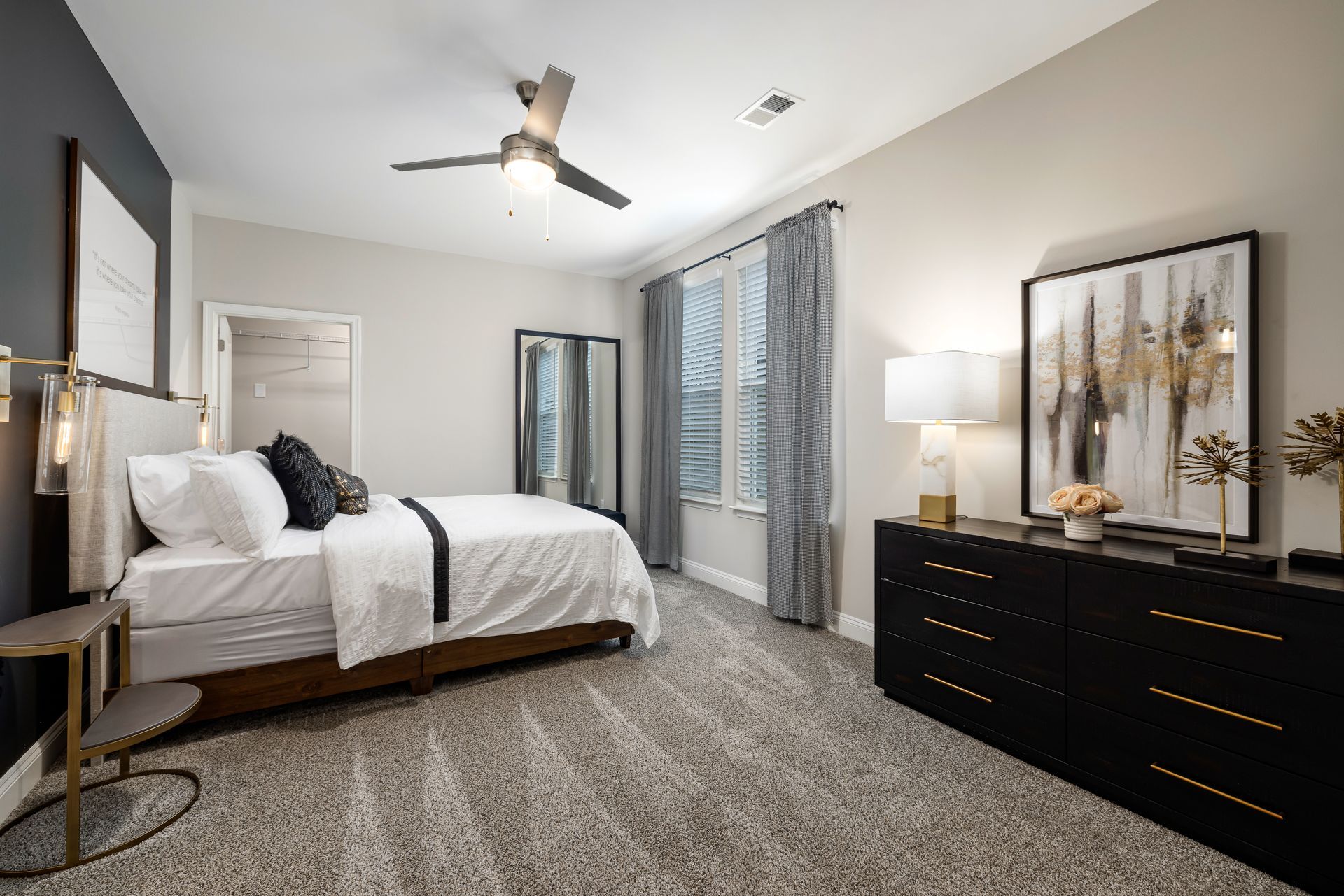 Modern bedroom with white bed, dark dresser, gray carpet, and large windows with curtains