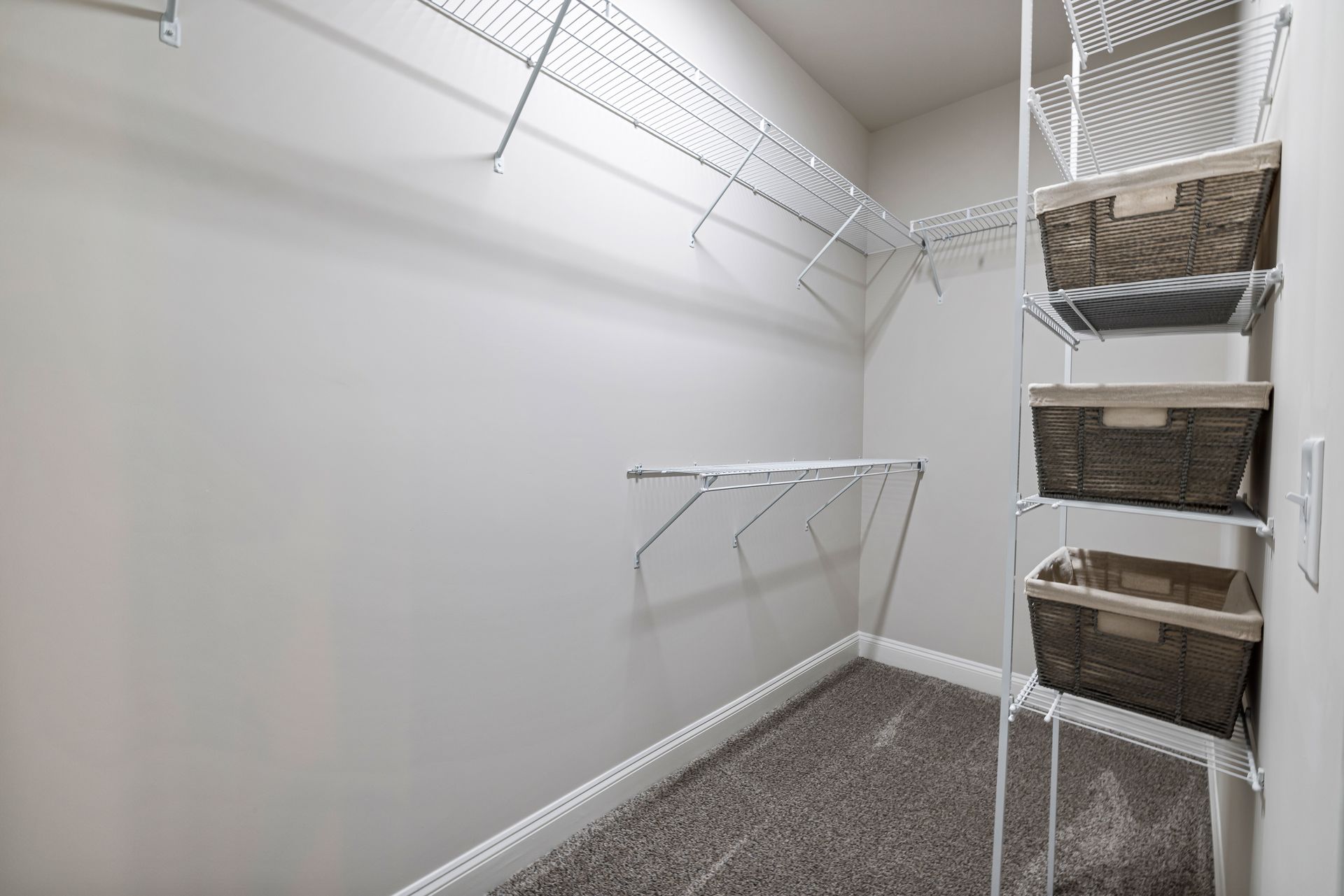 Empty walk-in closet with white walls, wire shelving, and woven baskets on the right.