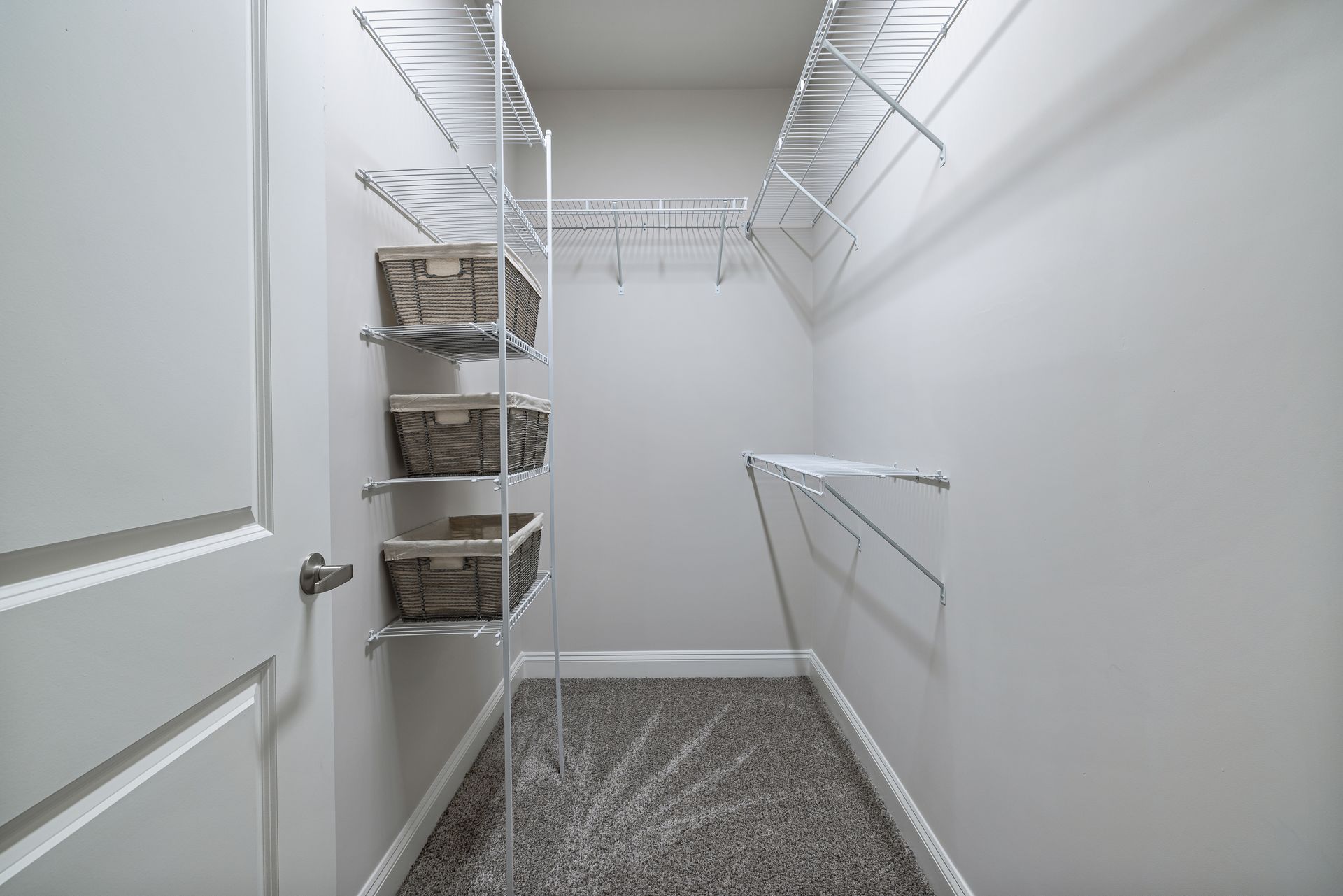 Empty walk-in closet with white wire shelving and carpeted floor.