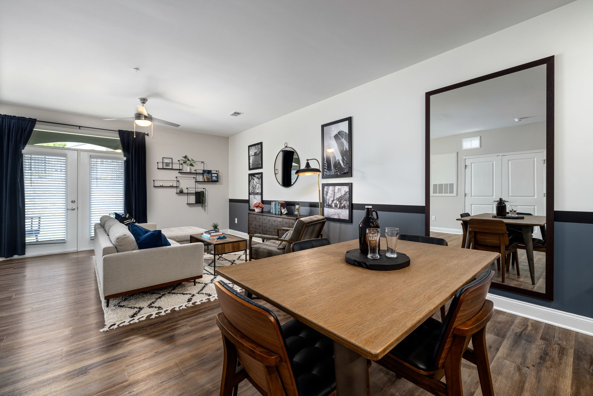 Open-concept living and dining room with white walls, dark wood table, couch, and large mirror above dining area