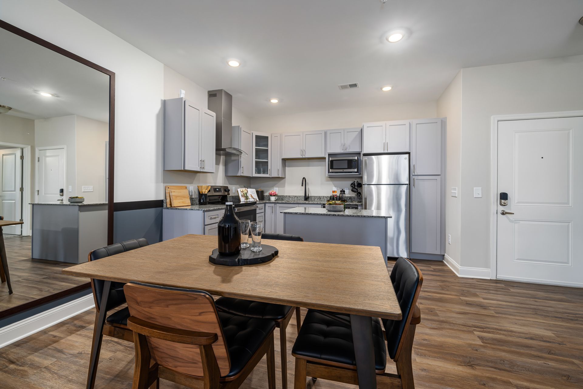 Modern kitchen and dining area with stainless appliances, granite island, and wood table by a large wall mirror