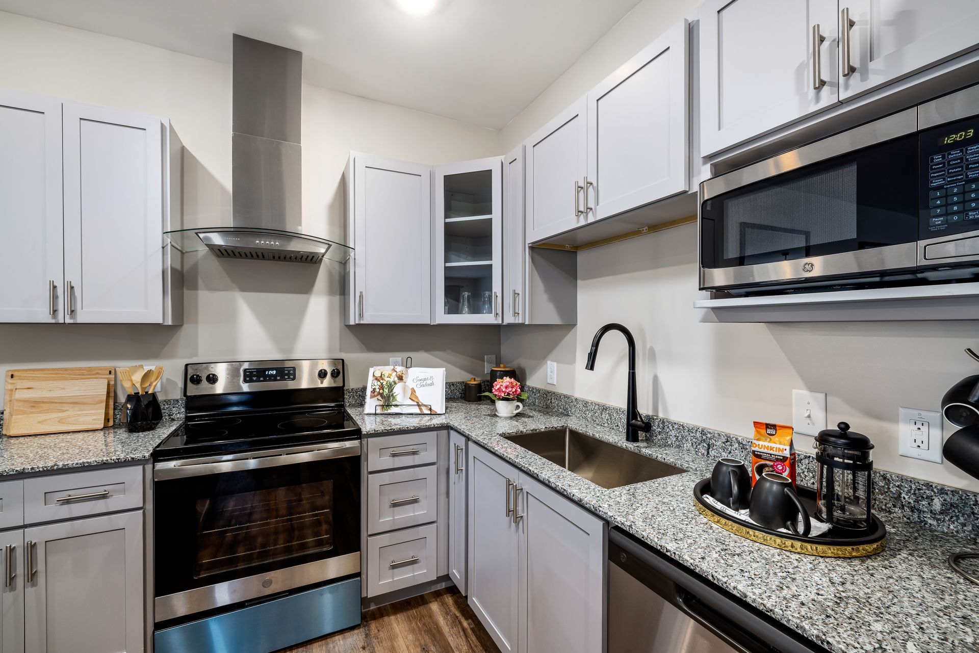 Modern white kitchen with stainless steel appliances, granite counters, and black sink faucet