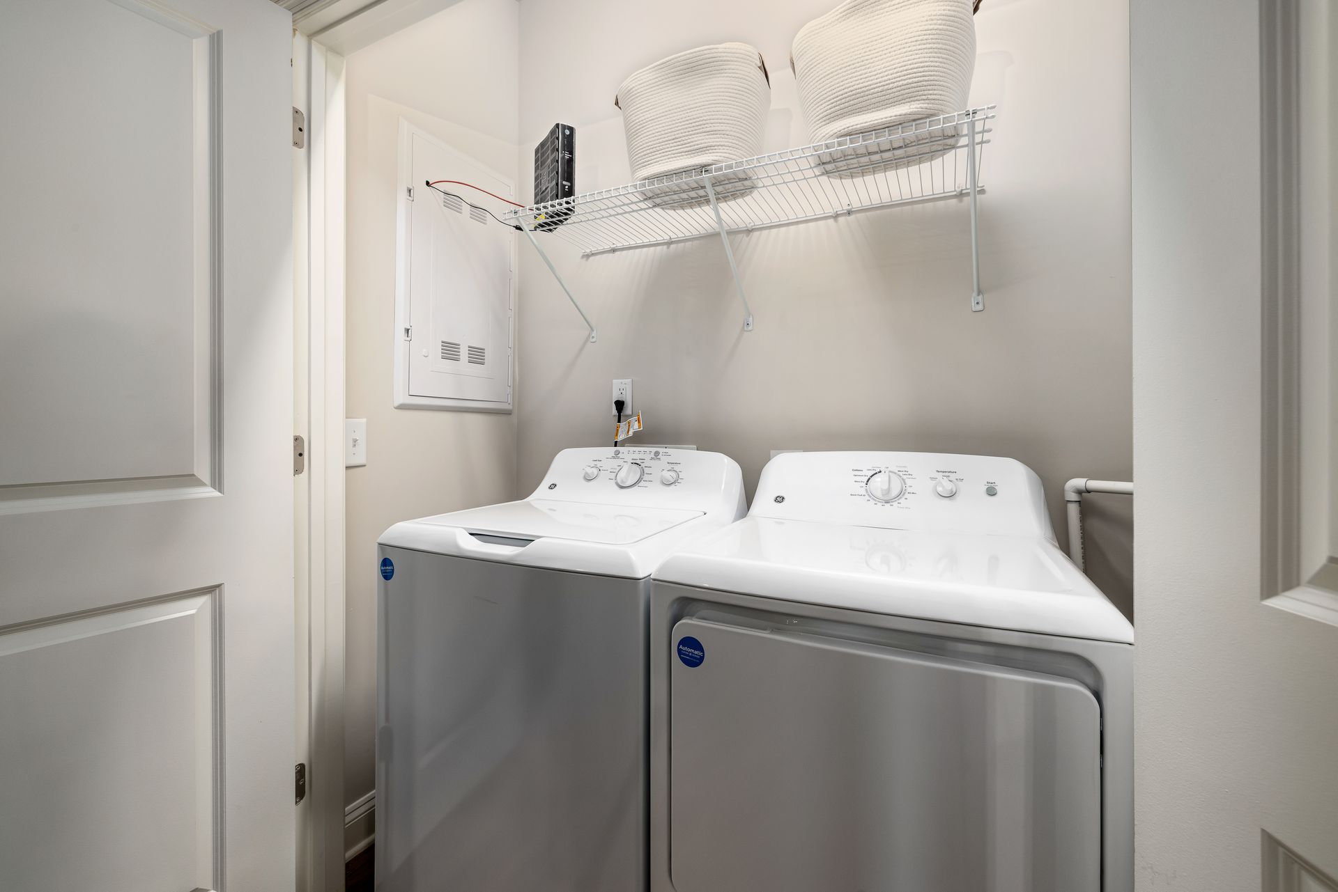Laundry room with a washer and dryer beneath wire shelves holding baskets