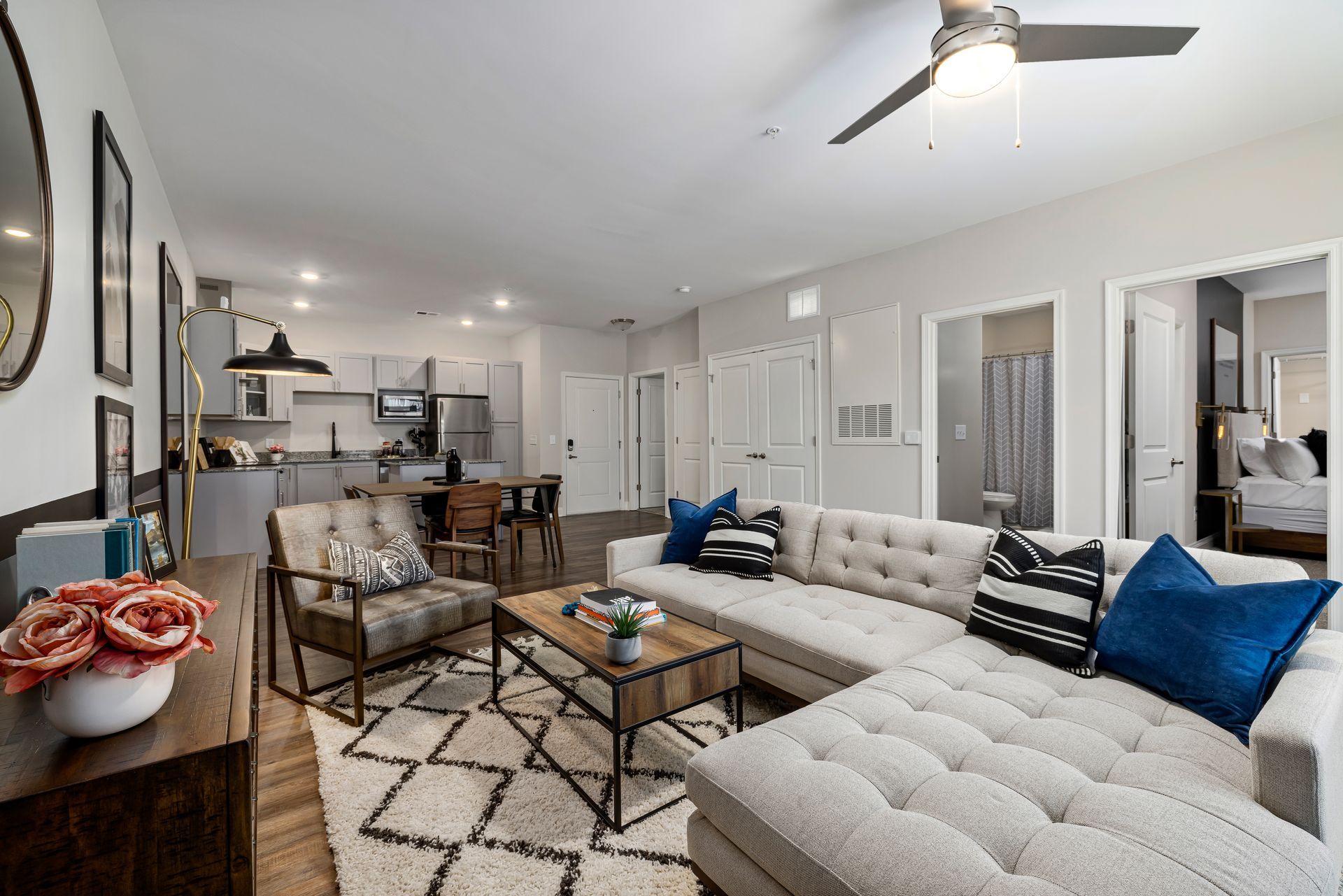 Modern living room with a white sectional sofa, patterned rug, and open view to the kitchen and dining area.