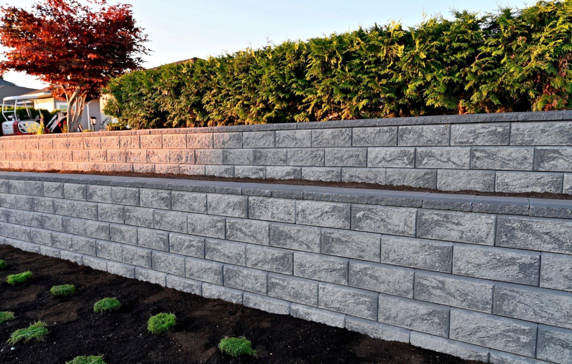 A close-up capture of a gray block stone retaining wall built as a two-tier wall into a landscape. A close-up capture of a gray block stone retaining wall built as a two-tier wall into a landscape.