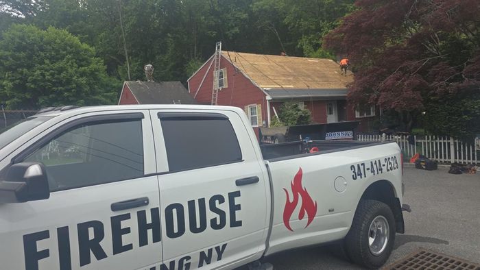 White FIREHOUSE pickup truck parked in front of a red building with trees in the background