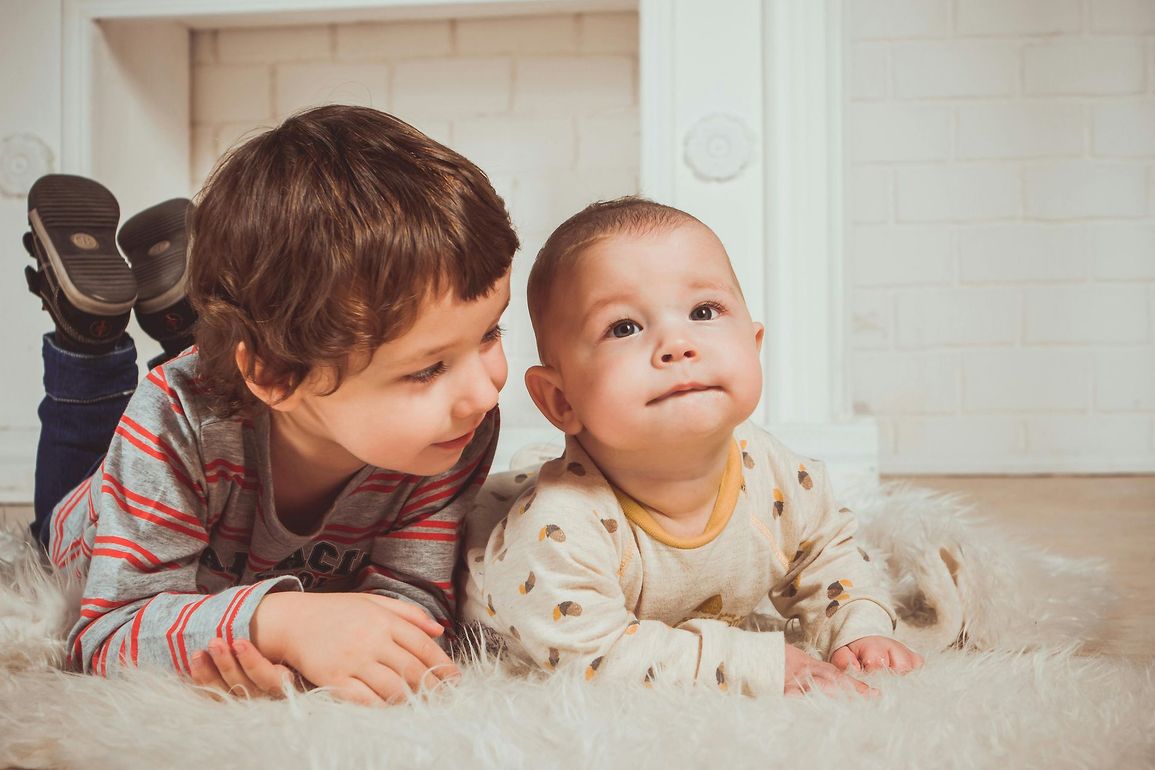A young boy in striped shirt and baby are laying on the ground next to each other, on their stomachs.