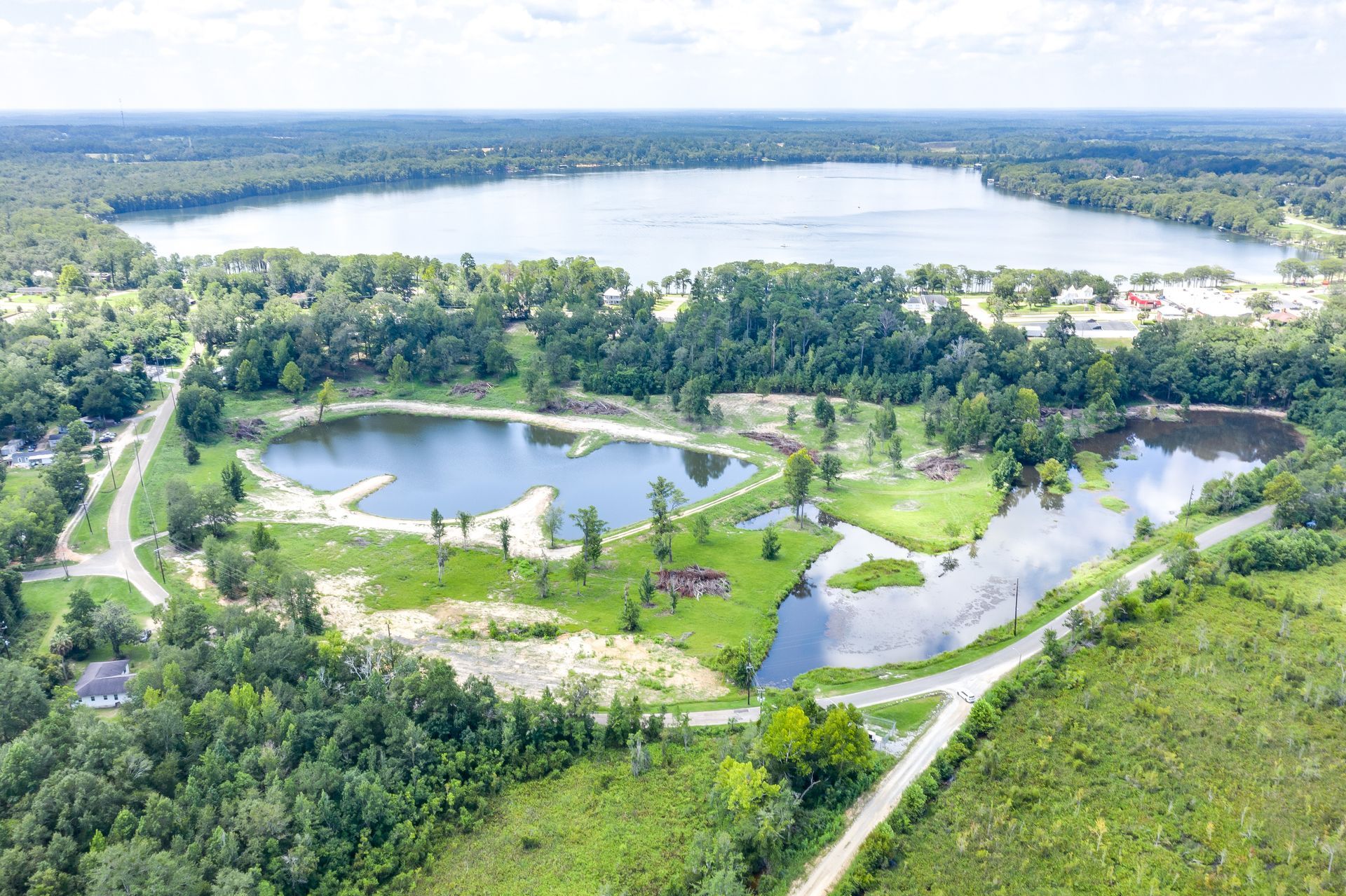 Aerial view of a park with small ponds, and a large lake surrounded by trees and greenery