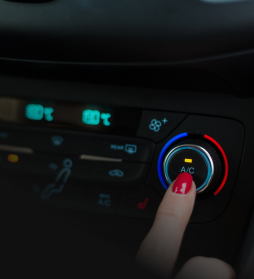 Finger pressing A/C button on a car climate control panel with blue and red temperature rings. | E&R Automotive