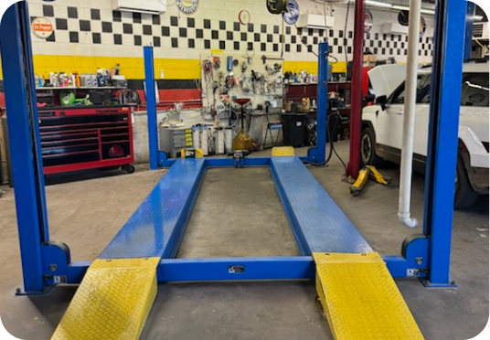 Blue auto lift in a garage with yellow ramps and workshop tools in the background | E&R Automotive
