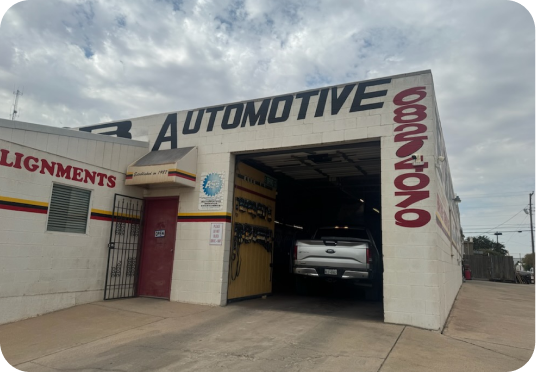 Auto body shop with a car inside a garage bay and red signage on the building | E&R Automotive