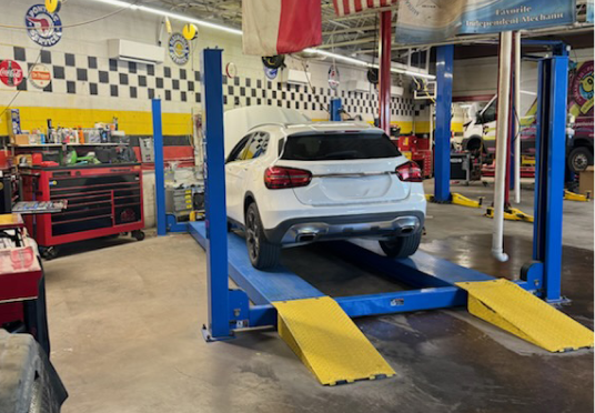 White SUV on a blue vehicle lift inside an auto repair shop with yellow ramps | E&R Automotive