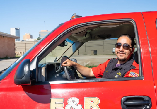 Man in sunglasses driving a red truck, smiling out the open window. | E&R Automotive