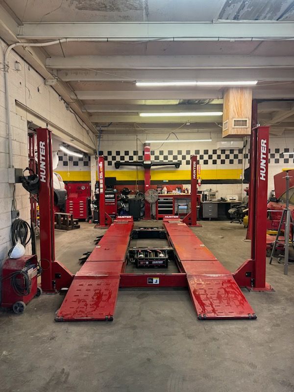 Auto repair shop with red car lift, tools, and checkered wall in the background | E&R Automotive