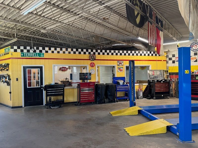 Auto repair shop interior with yellow walls, tool cabinets, and vehicle lifts under a high metal roof | E&R Automotive