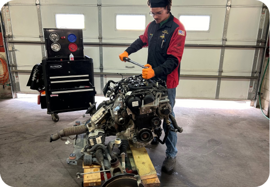 Mechanic in orange gloves inspecting a car engine on a pallet inside a garage | E&R Automotive