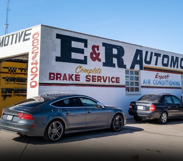 Gray sedan and black SUV parked outside E&R Automotive shop with brake service and air conditioning signs | E&R Automotive
